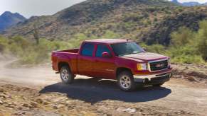 A red GMC Sierra 1500 pickup truck driving up a dirt road, mountains visible in the background.