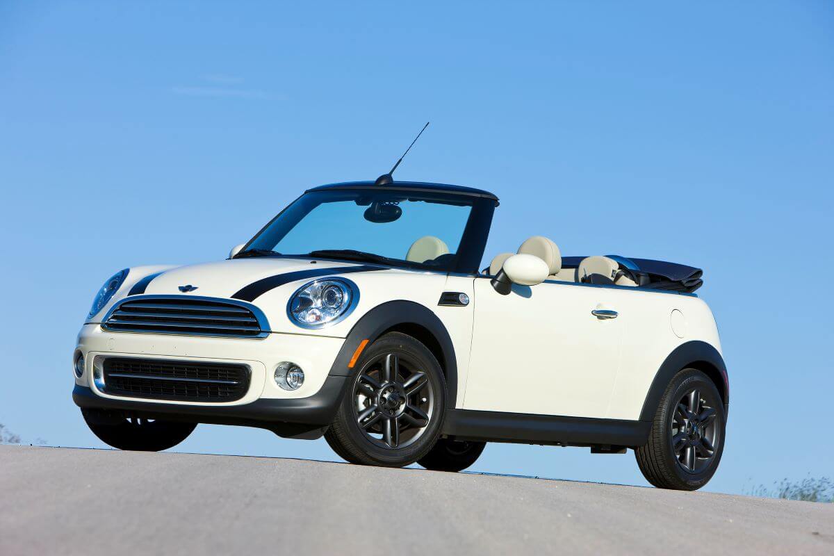 A white and black 2011 Mini Cooper Convertible model parked at the top of an asphalt hill road