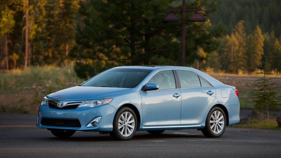 A used 2012 Toyota Camry Hybrid in blue cruises country roads.