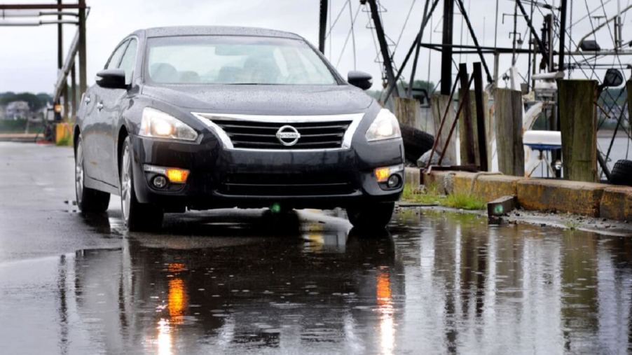 A black 2013 Nissan Altima cruises wet streets with questionable reliability.