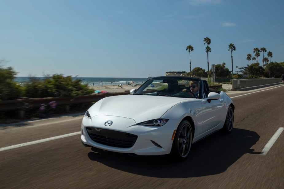 A new Mazda MX-5 Miata cruises a coastal road.