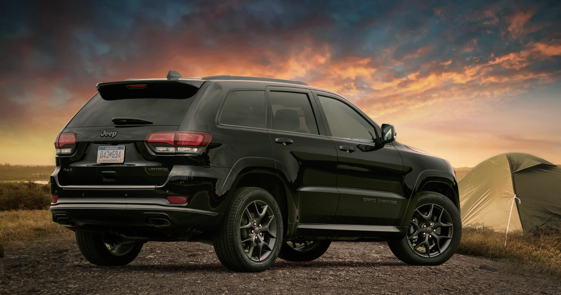 A black 2020 Jeep Grand Cherokee in front of a sunset with a tent in the background.
