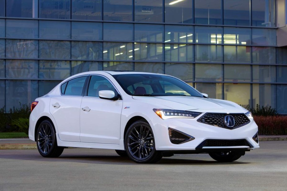 A white 2021 Acura ILX parked in front of a glass wall of a building. 