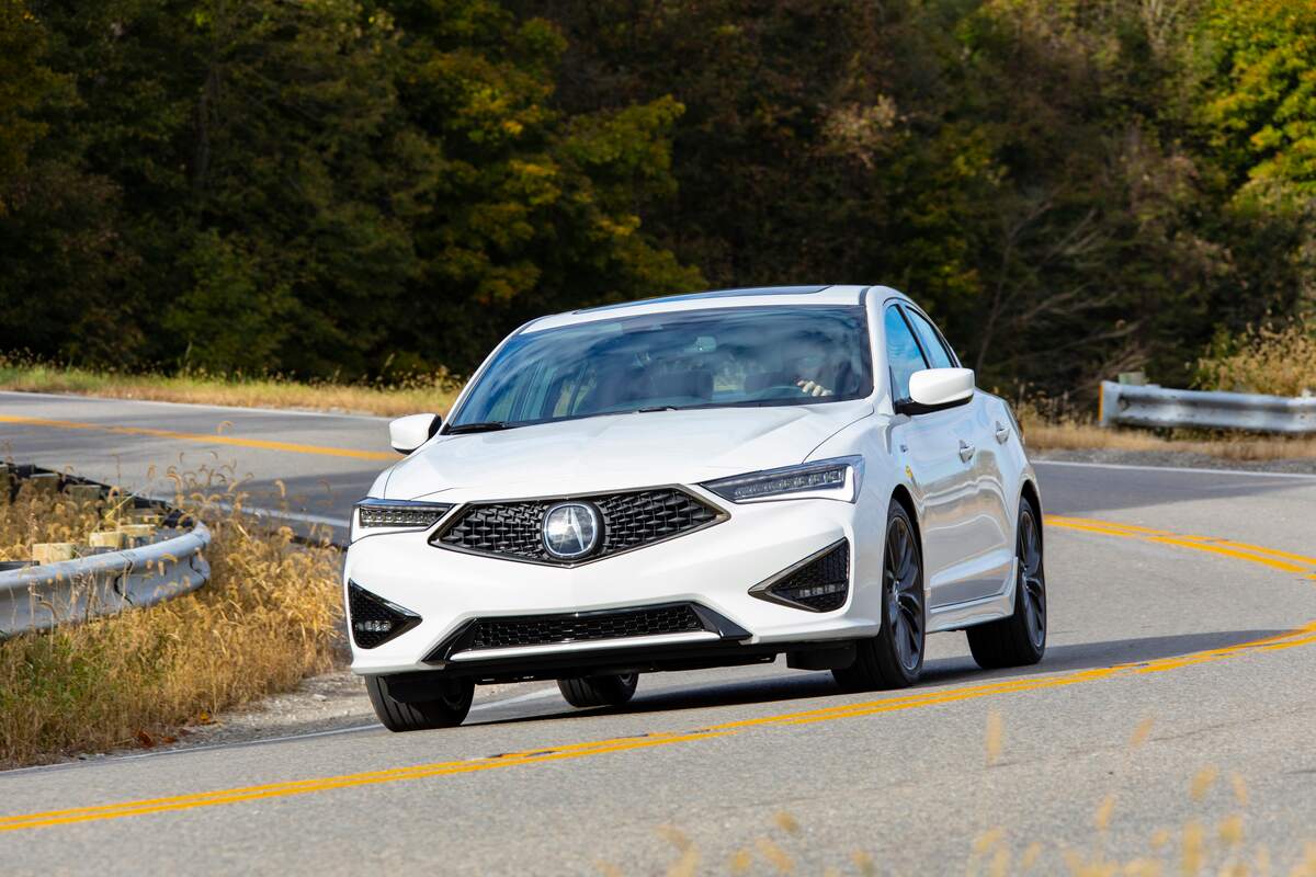 A white 2021 Acura ILX driving down a curvy road in a woody area.
