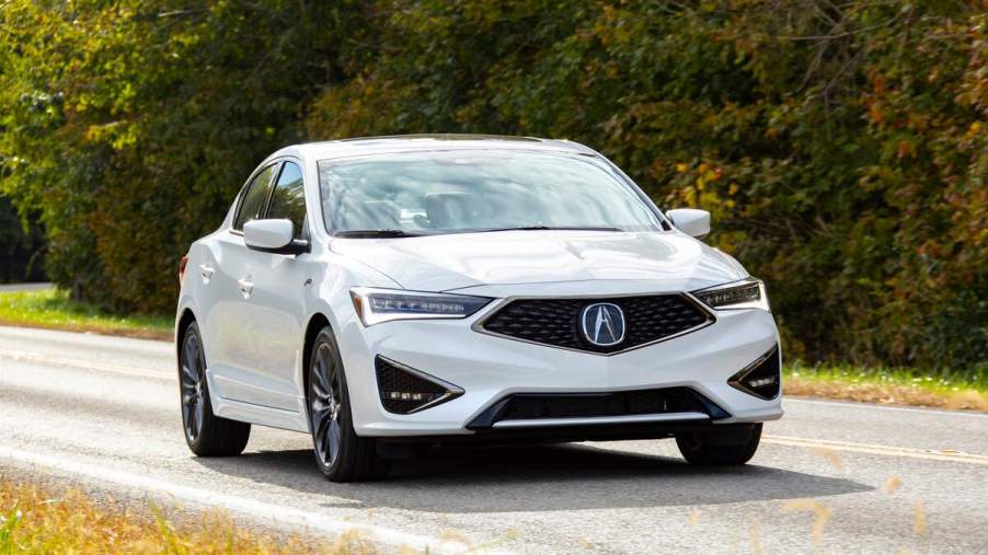 A white 2021 Acura ILX driving down a wooded country road.
