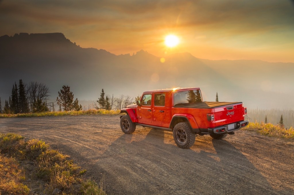 A red Jeep Gladiator pickup truck parked on a mountain trail, the sunsetting in the background.