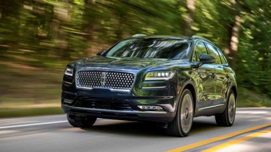 A 2021 Lincoln Nautilus Flight Blue midsize luxury SUV model driving on a forest highway