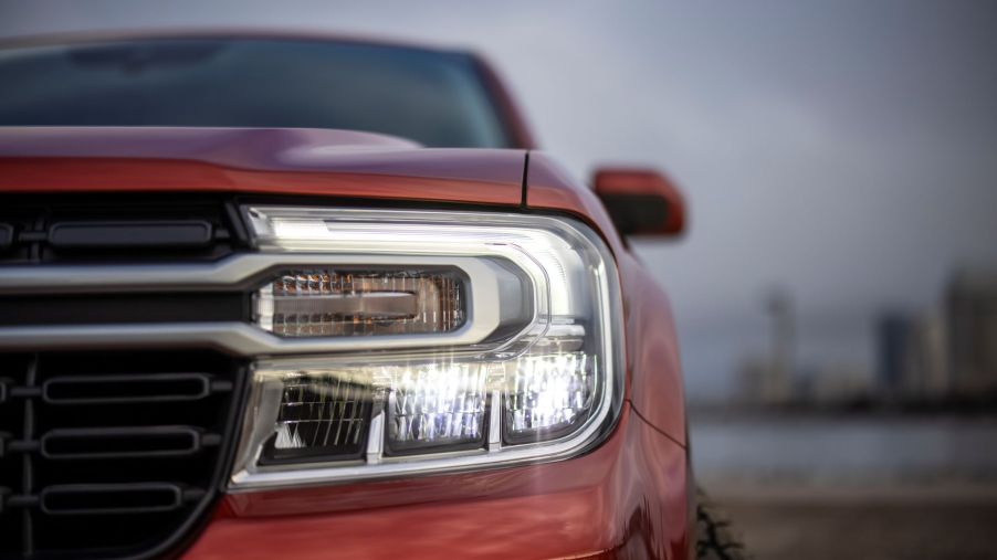 A closeup shot of a red-orange 2022 Ford Maverick Lariat compact pickup truck's headlights and grille