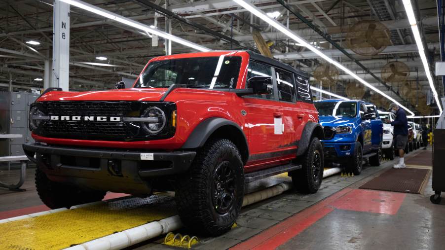 Red Ford Bronco rolls down an assembly line ahead of a blue Ford Ranger.