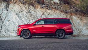 A red 2023 Cadillac Escalade, a full-size third-row luxury SUV that could be best for you, parked out doors in a rocky mountainous area.