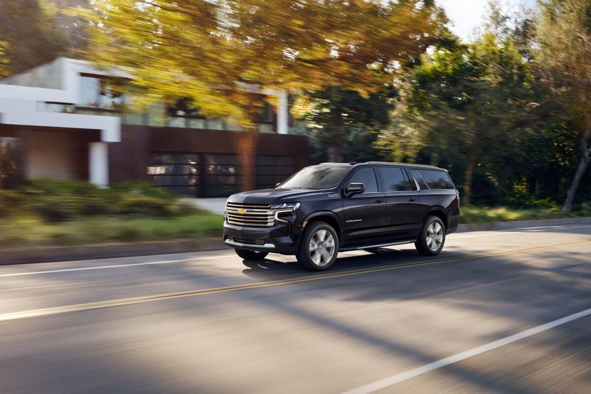 A black 2023 Chevy Suburban High Country full-size SUV model driving on a suburban neighborhood street