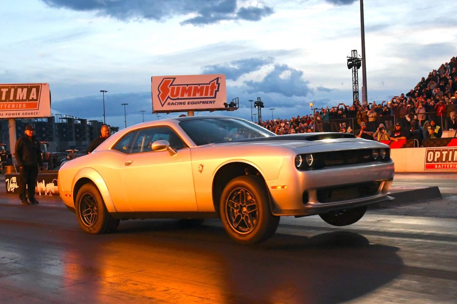 The SRT Demon 170 does a wheelie as it launches at a drag strip, a crowd visible in the background.