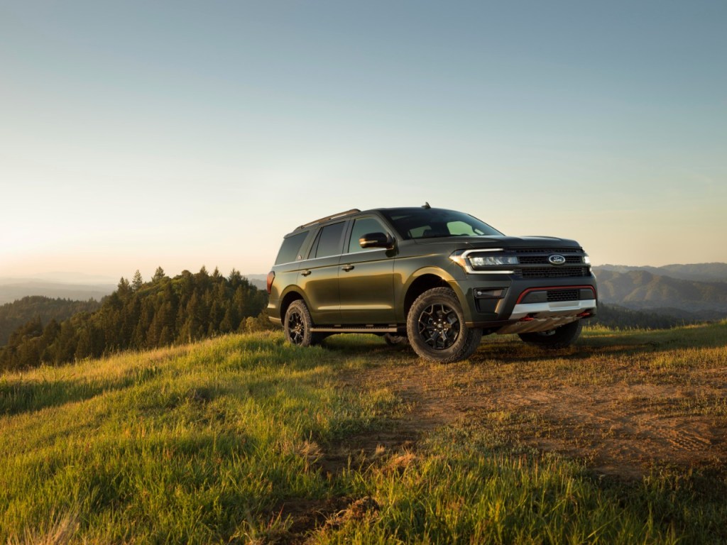 A green Expedition Timberline sits off-road on a grassy hill with sunset lighting. 