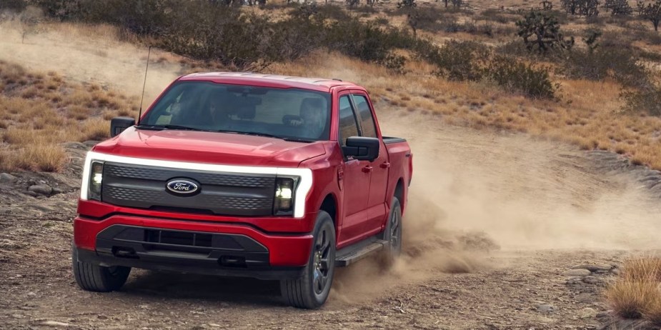 A red 2023 Ford F-150 Lightning is driving off-road. 