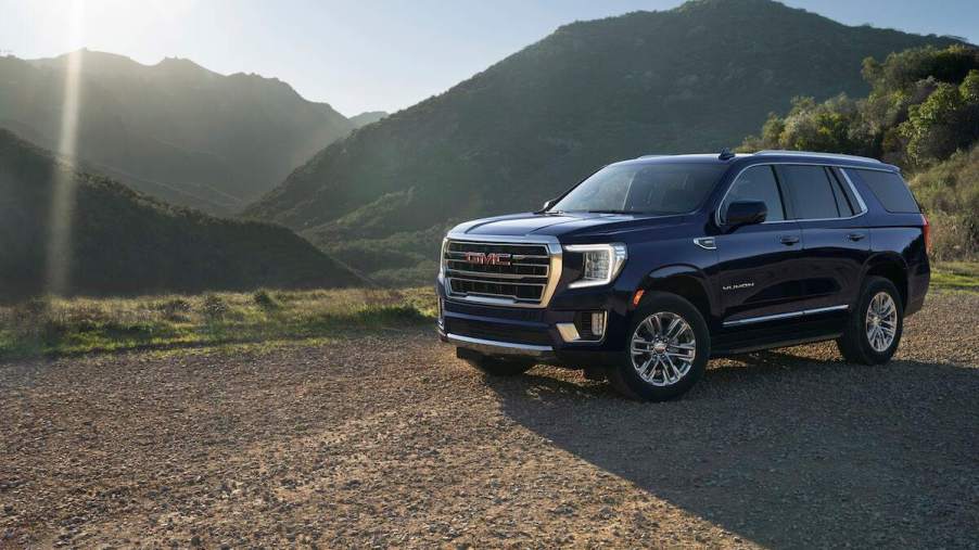 A dark blue 2023 GMC Yukon parked in front of a mountain scene.