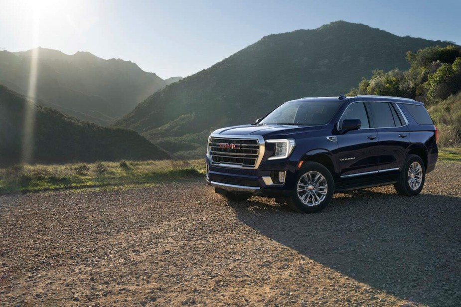 A dark blue 2023 GMC Yukon parked in front of a mountain scene.