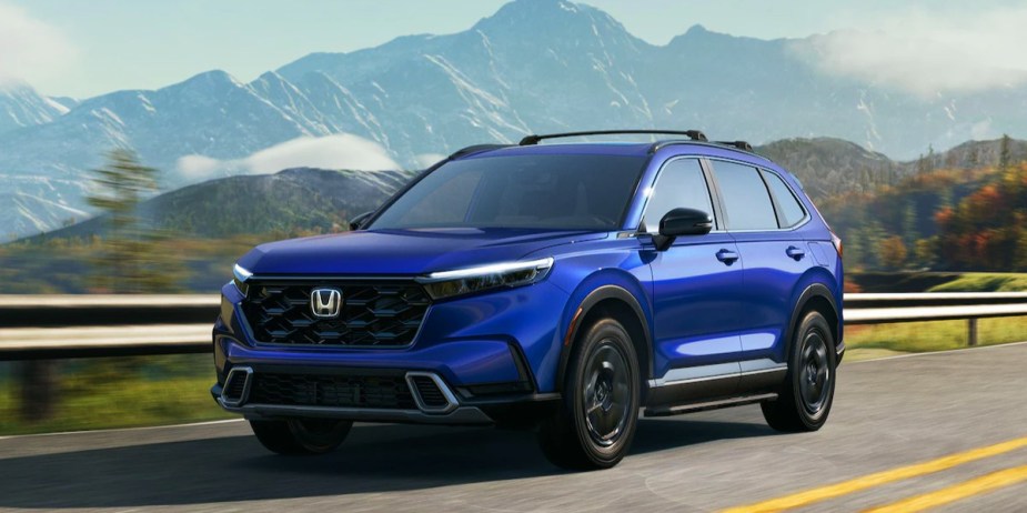 A blue 2023 Honda CR-V Hybrid small hybrid SUV is driving on the road. 
