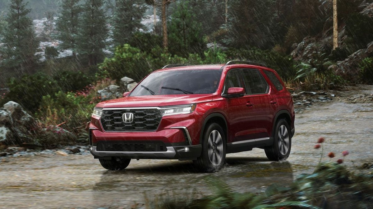 A red 2023 Honda Pilot driving outdoors in the rain.
