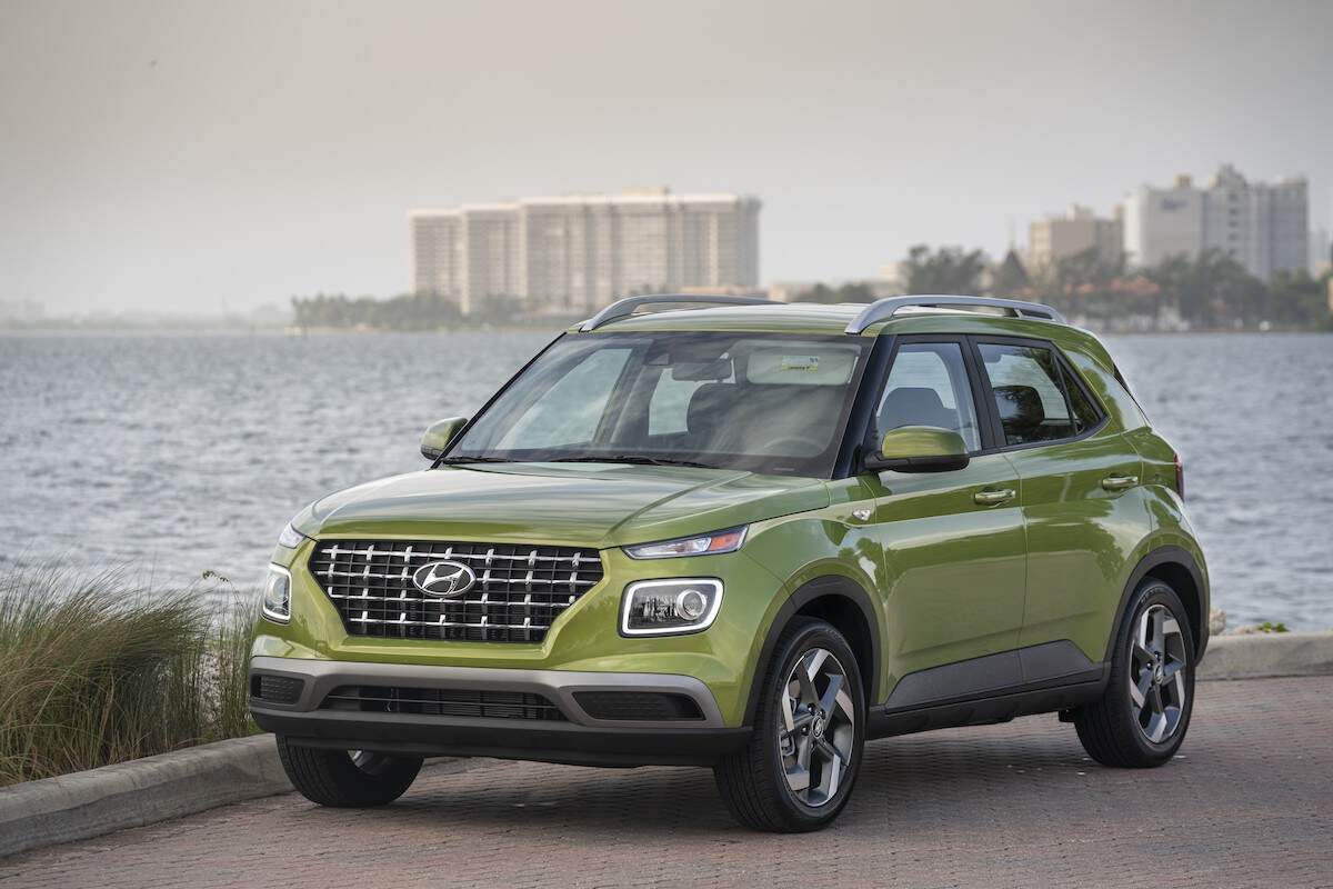 A light green 2023 Hyundai Venue parked in front of a large body of water with buildings in the background.