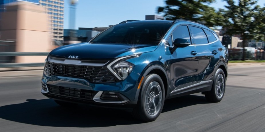 A blue 2023 Kia Sportage Hybrid small hybrid SUV is driving on the road. 
