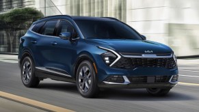 A blue 2023 Kia Sportage Hybrid small hybrid SUV is driving on the road.