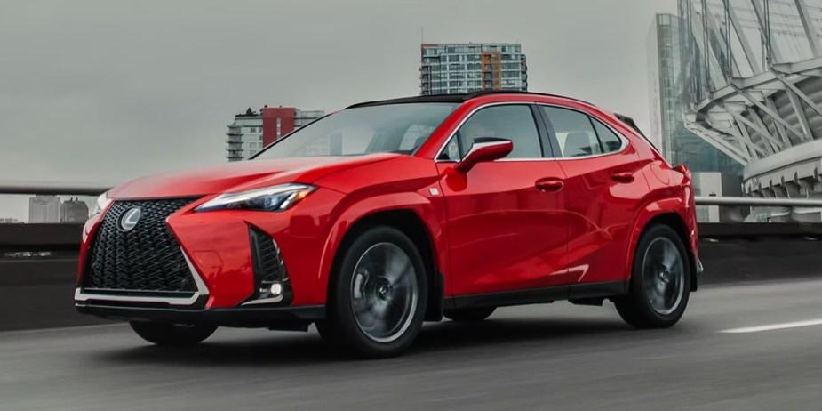 A red 2023 Lexus UX Hybrid subcompact hybrid SUV is driving on the road. 