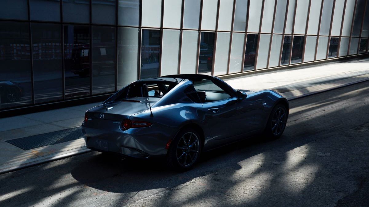 A 2023 Mazda MX-5 RF Hard Top Convertible roadster model covered in shadows from a glass-paneled wall