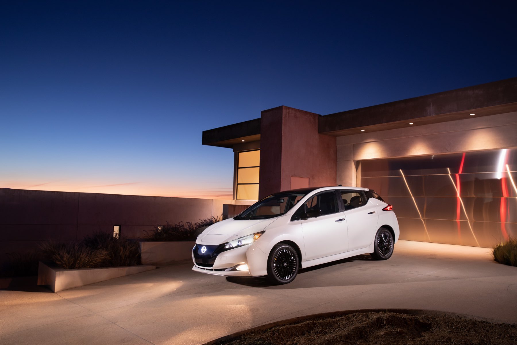 A white Nissan Leaf sits on a driveway at dusk.