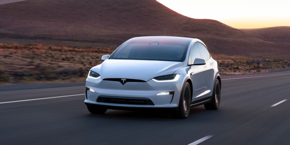 A white 2023 Tesla Model X midsize electric SUV is driving on the road. 