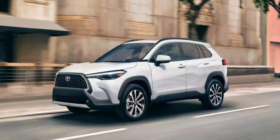A white 2023 Toyota Corolla Cross subcompact SUV is driving on the road.