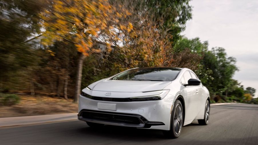 The all-new 2023 Toyota Prius drives down a road near some trees