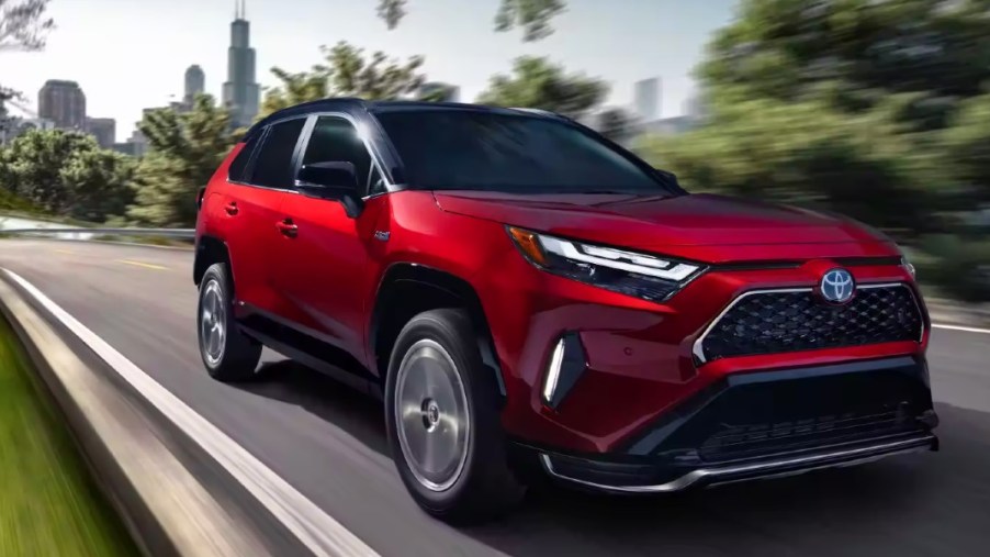 A red 2023 Toyota RAV4 Prime small plug-in hybrid SUV is driving on the road.