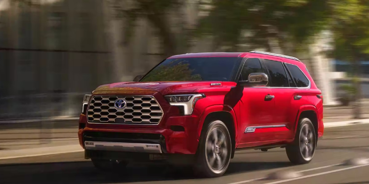 A red 2023 Toyota Sequoia full-size SUV is driving on the road.