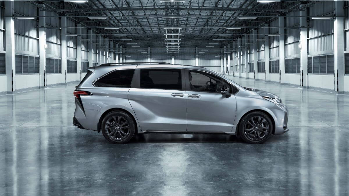 A side profile shot of a silver 2023 Toyota Sienna 25th Anniversary Edition hybrid minivan in an empty warehouse