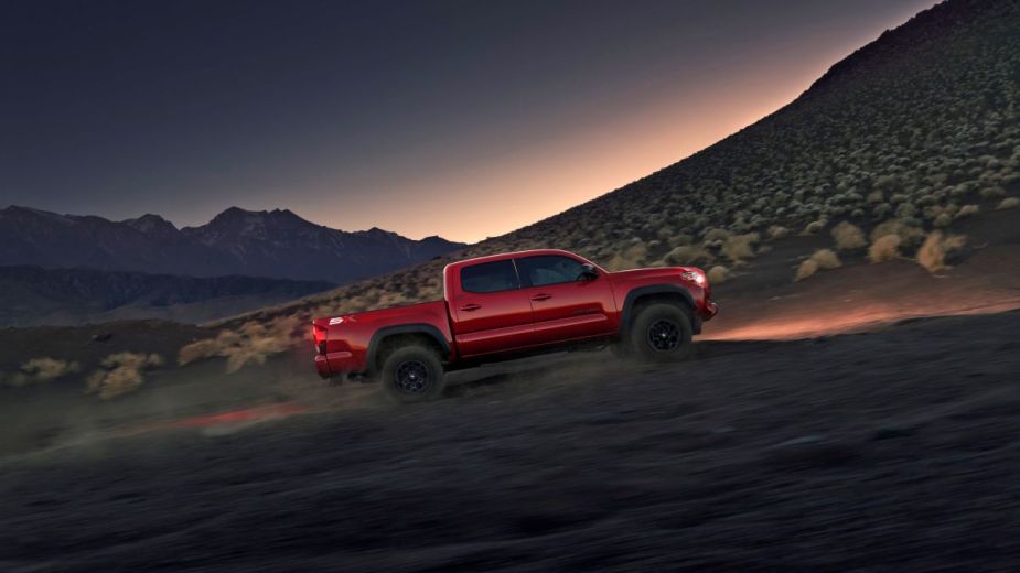A red 2023 Toyota Tacoma with SX Package midsize pickup truck climbing a desert mountain at dusk