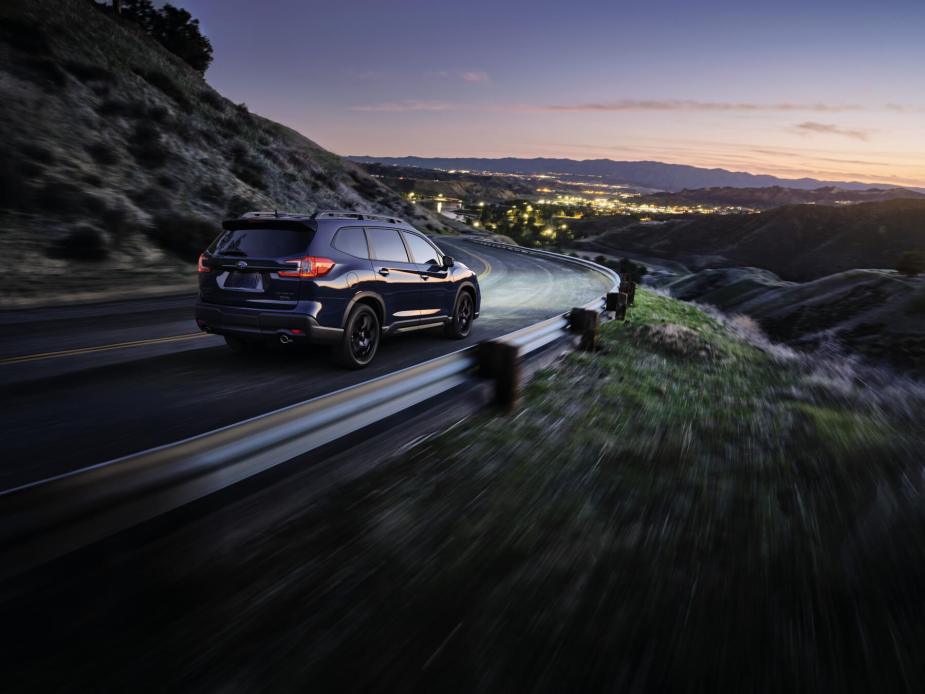 Rear view of a 2023 Subaru Ascent cresting a mountain road at sunset. 