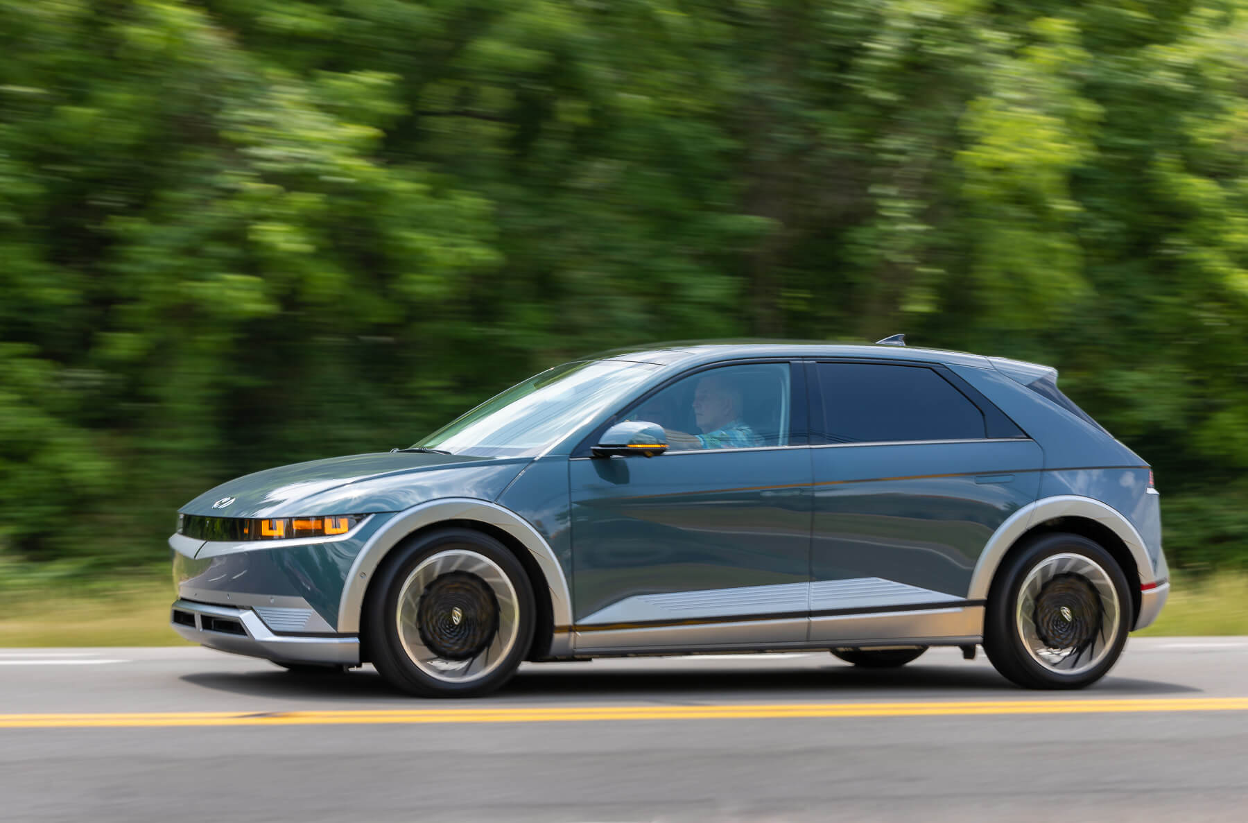 A 2023 Hyundai Ioniq 5 electric SUV rolls down a road with blurred greenery in the background. It's the lowest rated 2023 compact SUV according to J.D. Power