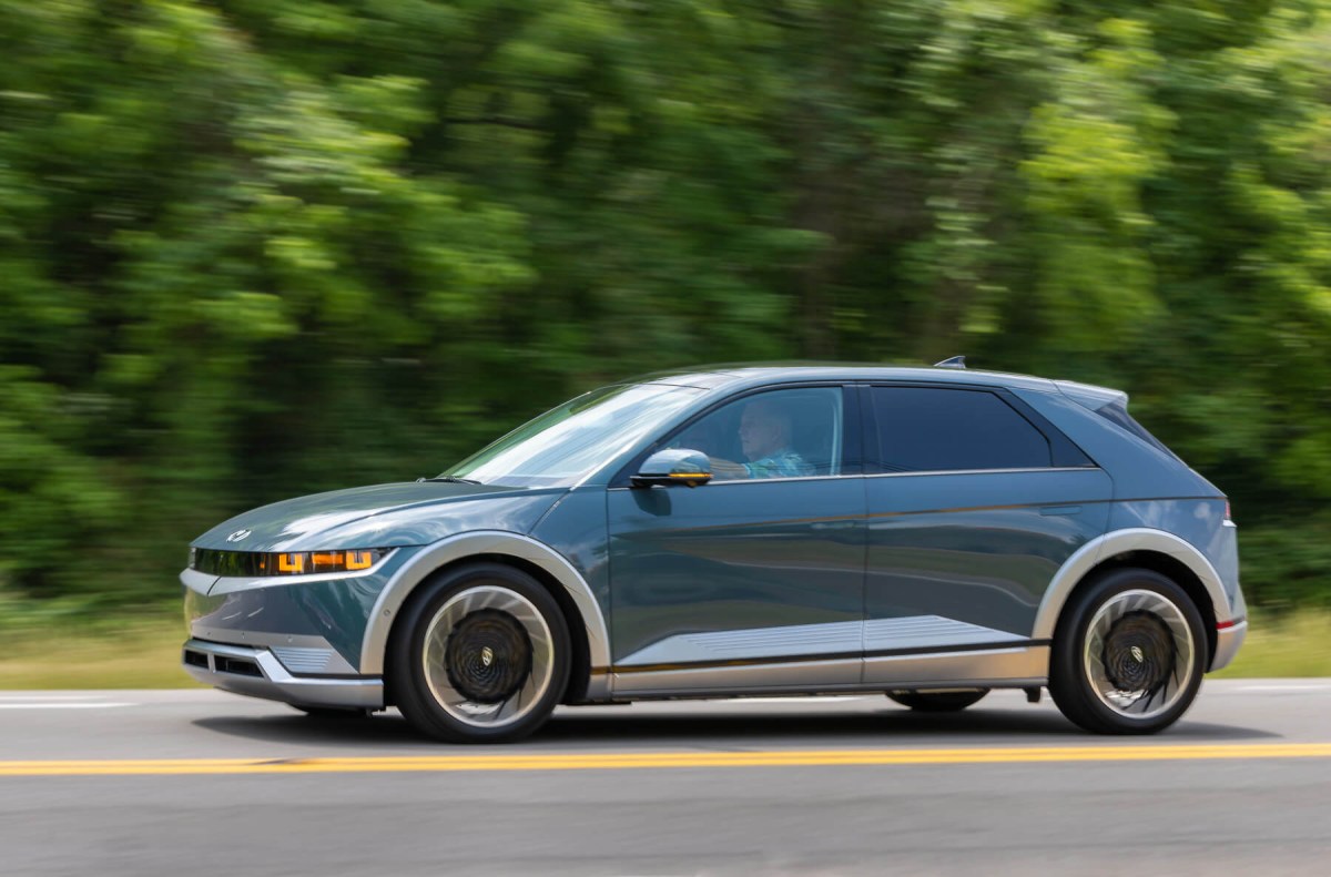 A 2023 Hyundai Ioniq 5 electric SUV rolls down a road with blurred greenery in the background.