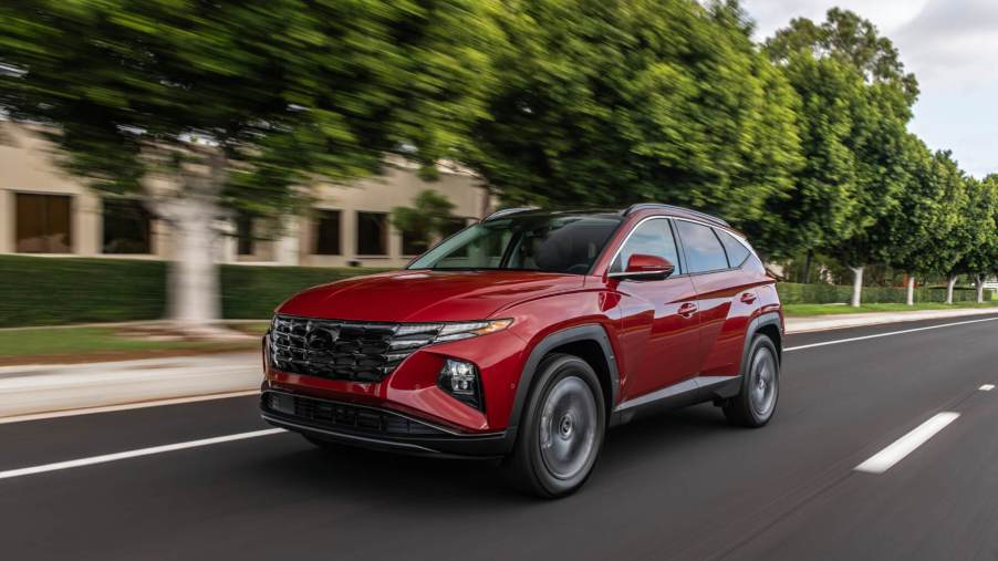 A red 2023 Hyundai Tucson SUV cruises down a road with green trees beside it. Hyundai has been cited as the year's best SUV brand.
