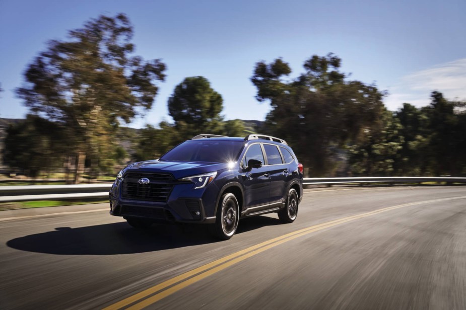 The 2023 Subaru Ascent three-row family SUV drives down a road with trees in the background.