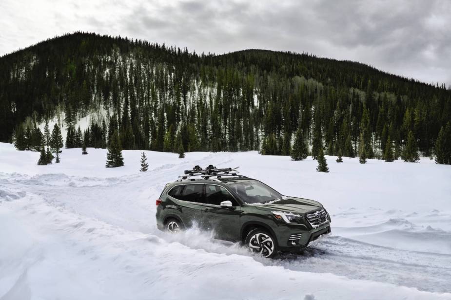 A green 2023 Subaru Forester, one of Kelley Blue Book's top resale value SUVs, drives through snow in front of a mountain.