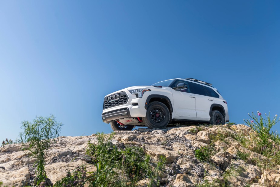 A white 2023 Sequoia drives on a rocky trail - view from below looking up with blue sky in background. 