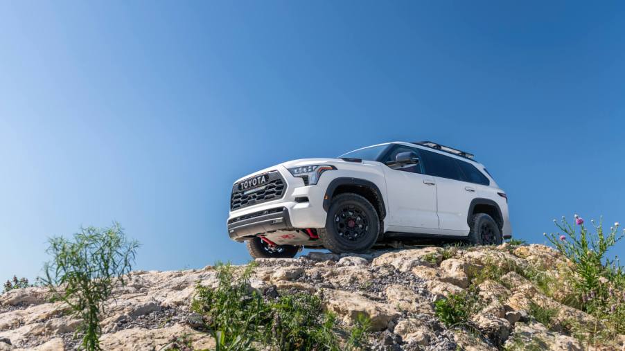 A white 2023 Sequoia drives on a rocky trail - view from below looking up with blue sky in background.