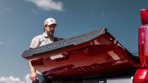 A man raises the tailgate on a red 2023 Toyota Tundra full-size pickup truck, blue sky visible in the background.