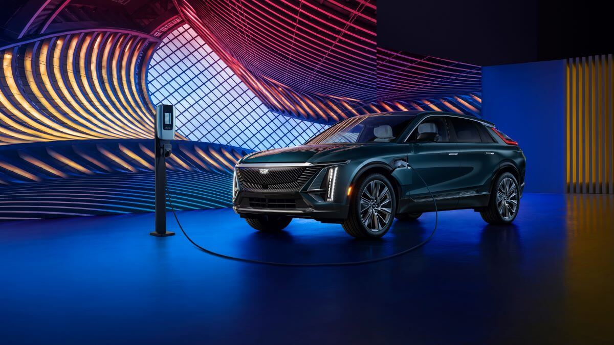 A blue-green 2024 Cadillac Lyriq electric luxury SUV model plugged in and charging in a mood light showroom.