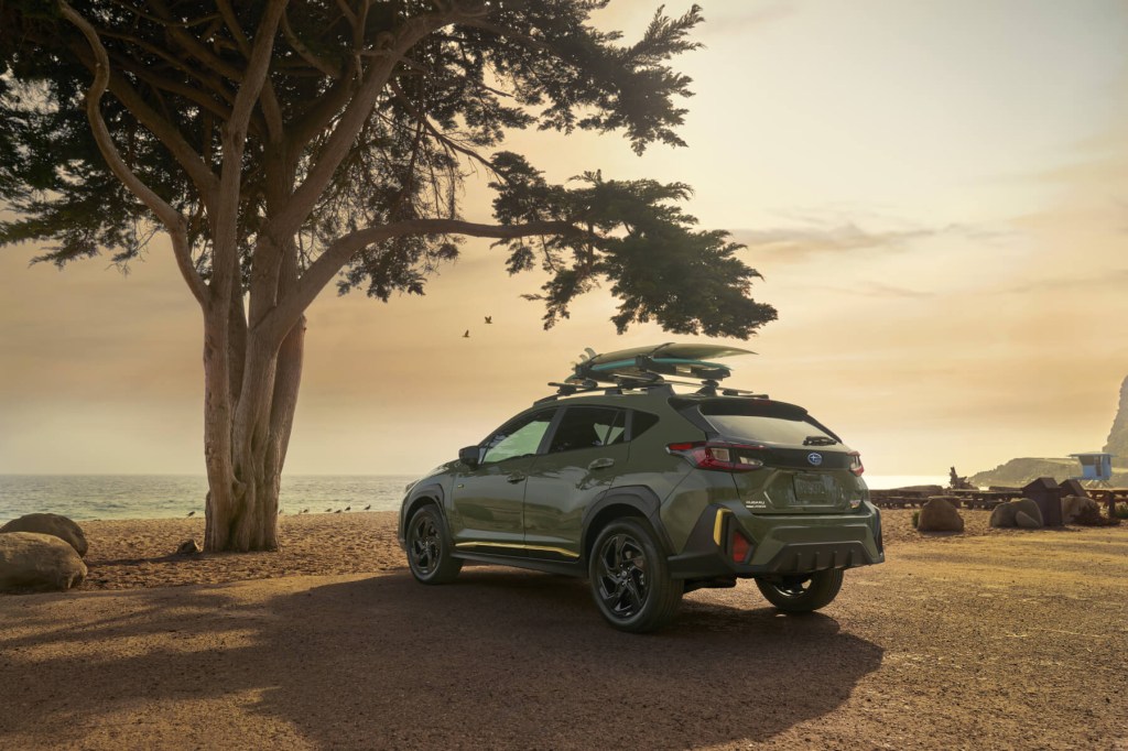 The rear of a 2024 Subaru Crosstrek sits with a tree in the foreground and a sunset in the background. 