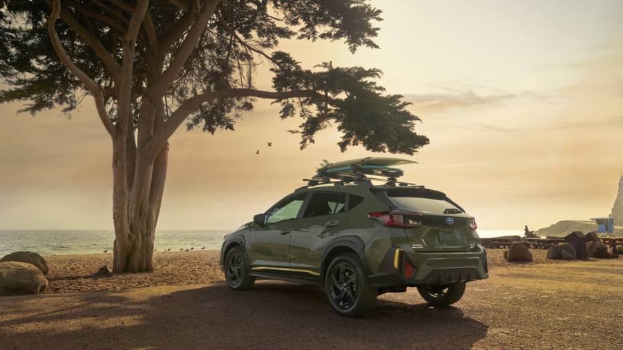 The rear of a 2024 Subaru Crosstrek sits with a tree in the foreground and a sunset in the background.