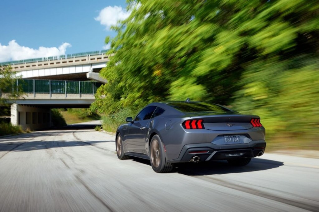 A gray 2024 Ford Mustang EcoBoost Premium blasts down a road next to a park. 
