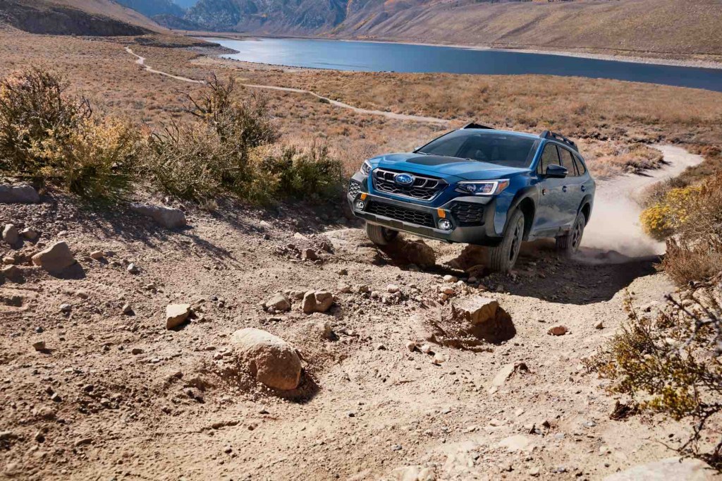 A blue Subaru Outback Wilderness climbs up a rocky slope.