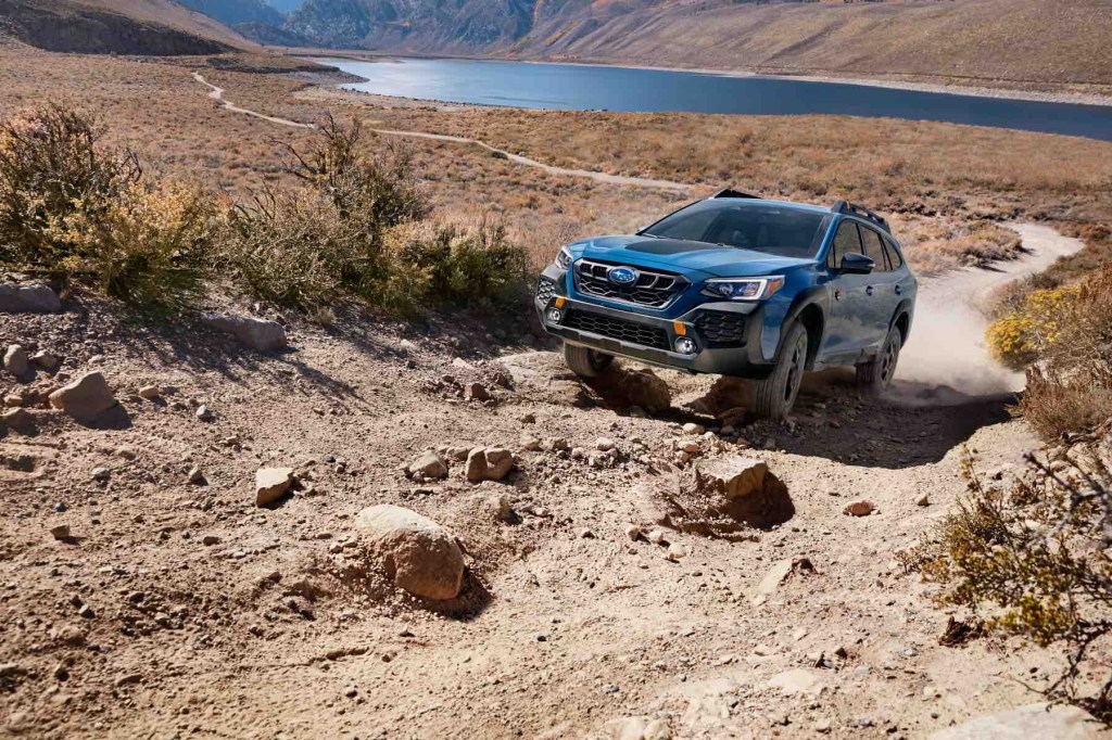A blue Subaru Outback Wilderness climbs up a rocky slope. 